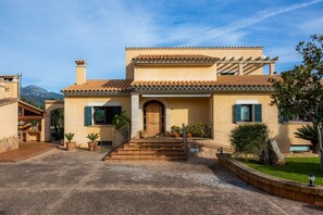 Een gebouw in mediterrane stijl met een betegeld dak, een centrale ingang met treden en een met stenen bestraat binnenterrein.