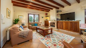 Ein Wohnzimmer mit Sofa, Couchtisch, Kamin, Fernseher und Holzbalken an der Decke.