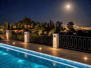 Une piscine offrant une vue nocturne sur le paysage urbain et les arbres.