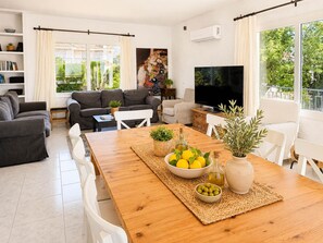 Ein modernes Wohnzimmer mit Sofa, Fernseher und Essbereich, dessen Tisch mit Zitronen und Oliven dekoriert ist.