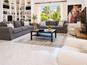 A living room with two grey sofas, a coffee table, a bookshelf, a television, and a painting. - Villa with private pool & casita + sea views (Mijas Costa)