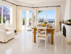 Un coin repas avec une table dressée pour quatre personnes, un canapé blanc et une vue sur la mer grâce à de grandes fenêtres.