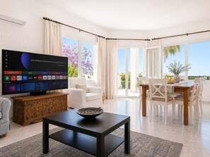 A modern living room with a flat-screen TV, a dining area with a table and chairs, and large windows offering a view of the outdoors. - Villa with private pool & casita + sea views (Mijas Costa)