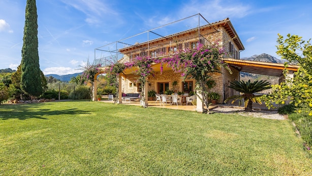 A stone house with a balcony, surrounded by a well-maintained lawn and a tall tree. - Charming Villa with Mountain Views, Wi-Fi & Air Conditioning in Selva (Selva)