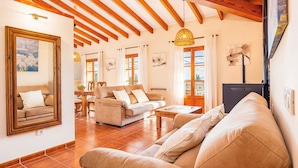 A spacious living area with a wooden ceiling, a sofa, a coffee table, and a dining table with chairs. - Charming Villa with Mountain Views, Wi-Fi & Air Conditioning in Selva (Selva)