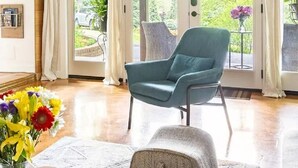 Une pièce comprenant un fauteuil turquoise, un pouf gris et une table basse en bois sur laquelle est posé un vase de fleurs.