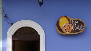 Una entrada con un arco blanco que conduce a un interior oscuro, una pared azul y un cartel con una ilustración de frutas.
