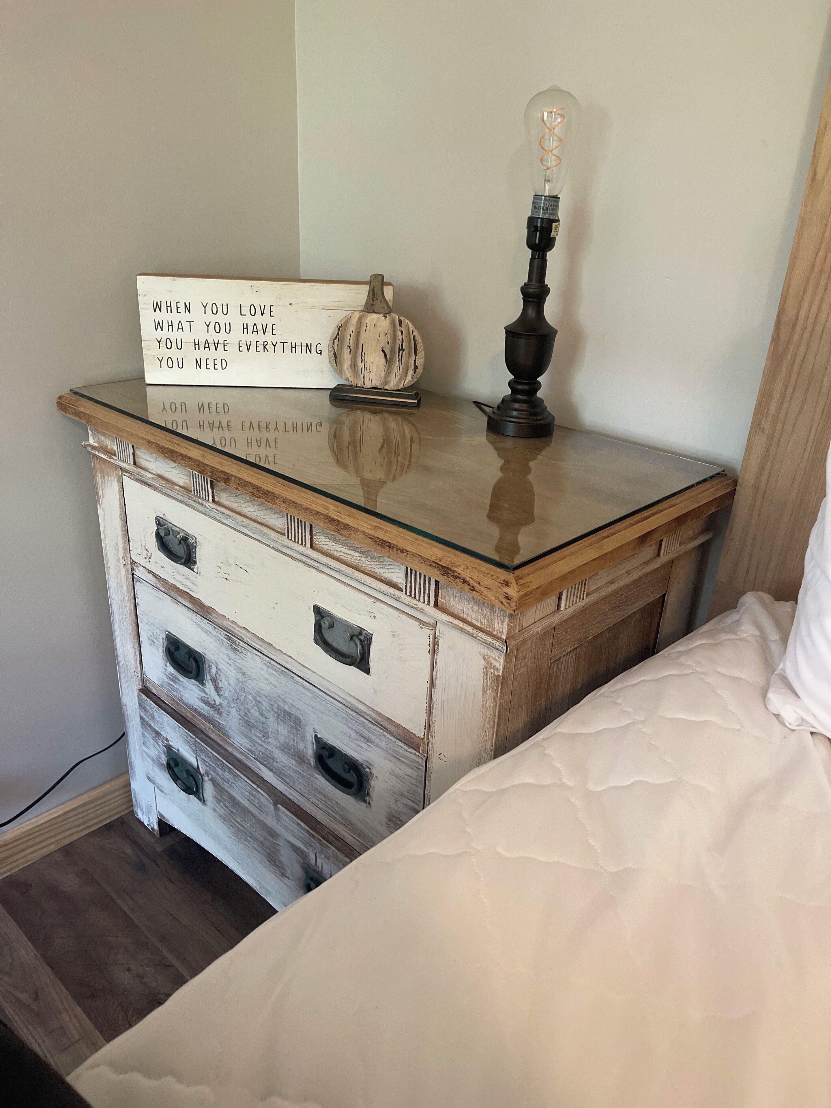 Une chambre avec une table de chevet en bois, une lampe, un panneau et une décoration en forme de citrouille.