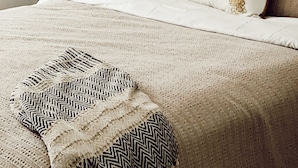 Uma cama com cabeceira de madeira, roupa de cama branca e almofadas estampadas.