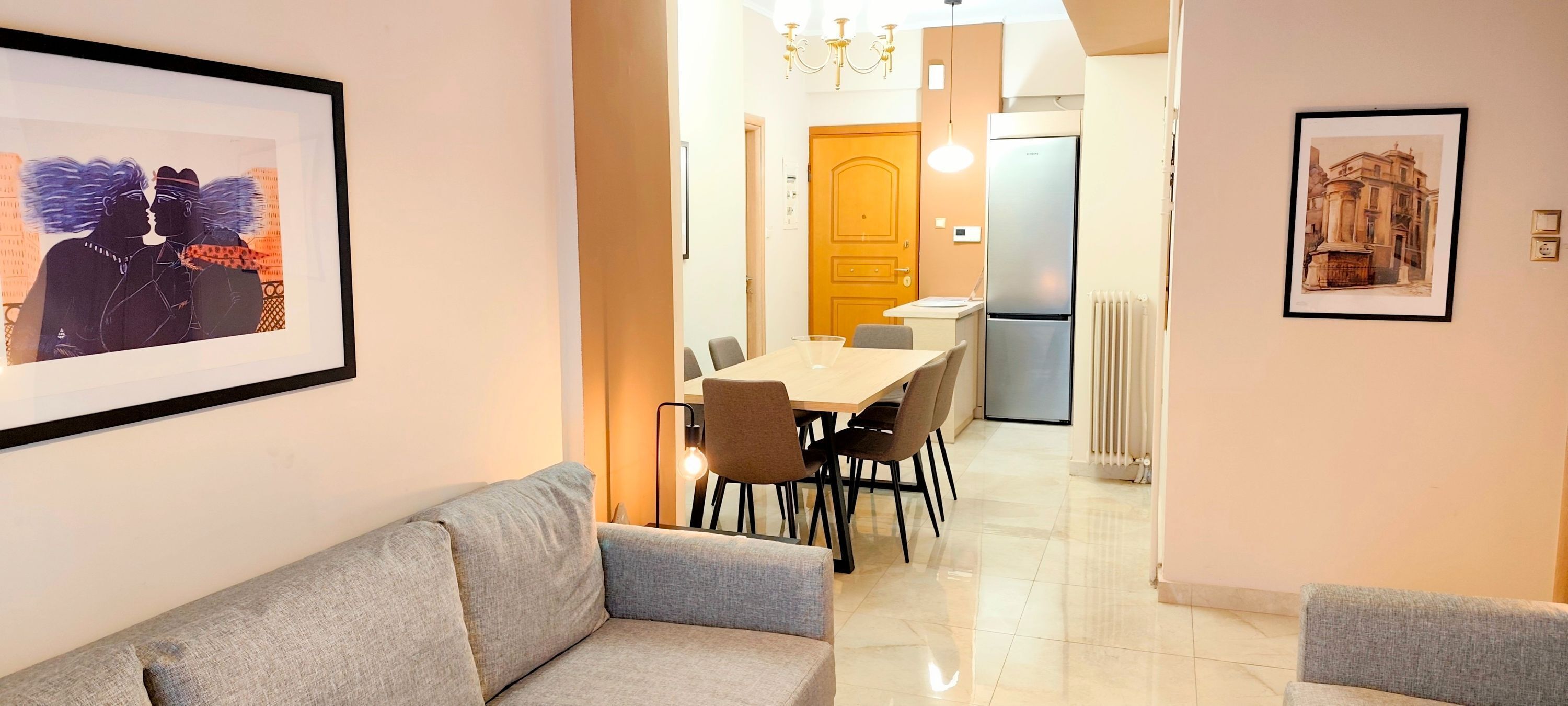 A modern interior with a sofa, dining table, chairs, framed artwork, and a refrigerator.
