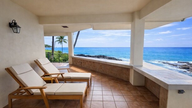 Een balkon met twee houten lounge fauteuils en uitzicht op de oceaan.
