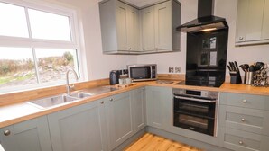 A modern kitchen with grey cabinets, a wooden countertop, a stainless steel sink, a microwave, an oven, and a black range hood. - Annies Farm Cottage (Londonderry)