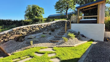 A garden with a stone wall, a wooden deck, and a grassy area.