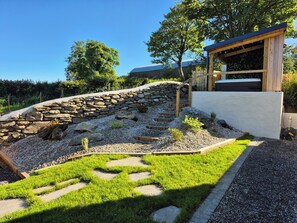 A garden with a stone wall, a wooden deck, and a grassy area. - Annies Farm Cottage (Londonderry)