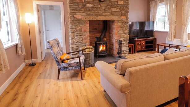 A cozy living room with a stone fireplace, a comfortable sofa, a chair, and a television. - Annies Farm Cottage (Londonderry)