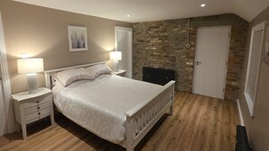 A bedroom with a bed, nightstands, a radiator, a stone wall, and a door. - Annies Farm Cottage (Londonderry)