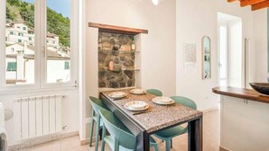 Un coin repas avec une table dressée pour quatre personnes, une étagère en pierre et une vue sur les bâtiments par une fenêtre.