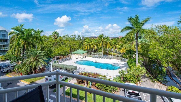 A pool surrounded by palm trees and a building with a green roof. - The Barbados | Private Balcony, Pool View! (Key West)