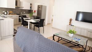 Un appartement moderne comprenant une cuisine, un coin repas et un salon. Il est équipé d’un canapé, d’une table à manger, de chaises, d’un téléviseur et d’une plante en pot.
