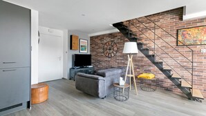 Un salón moderno con un sofá gris, un televisor, una lámpara y una pared de ladrillo con una escalera.