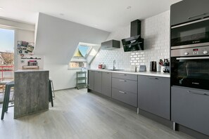 Une cuisine moderne avec des meubles gris, un four Bosch et une fenêtre donnant sur l’extérieur.