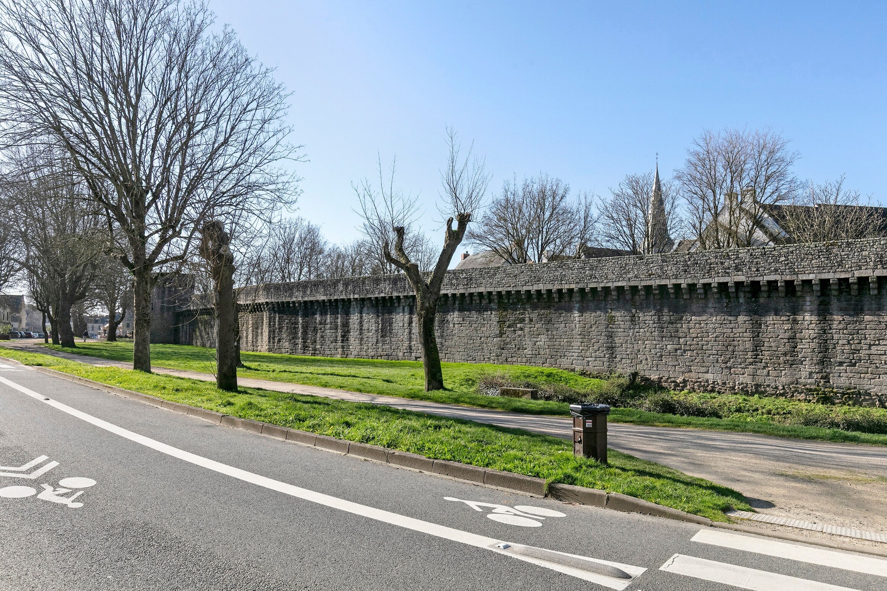 Eine Straße mit Radweg, einer Grünfläche und einer Steinmauer.