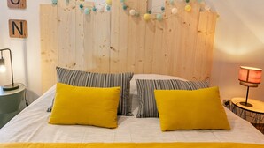 Una cama con almohadillas amarillas, un cabecero de madera y una guirnalda de bolas de colores.
