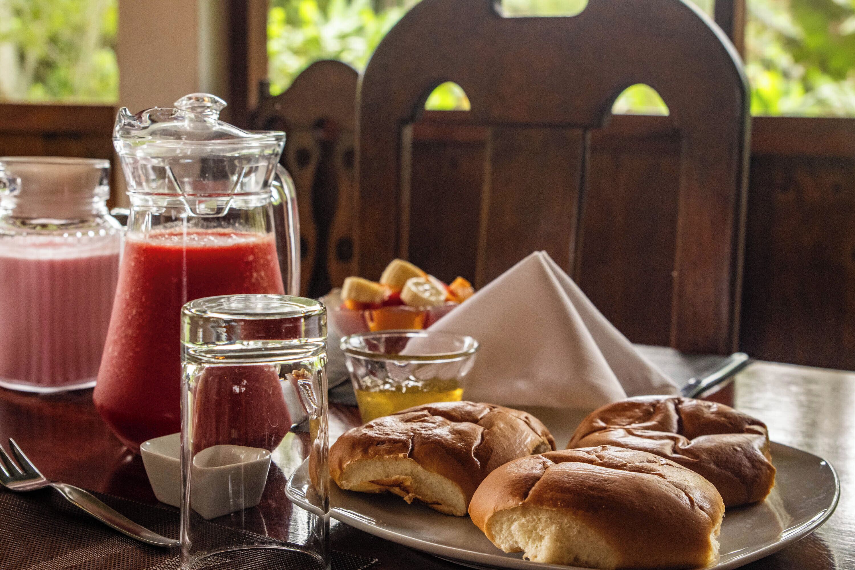 A table with a pitcher of red juice, a glass of water, a small bowl of honey, and two rolls of bread.