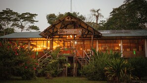 A rustic lodge with a sign reading "CHUNCHO LODGE" and a large windowed front area. - CHUNCHO LODGE (Tambopata)