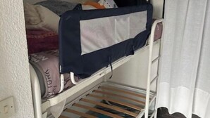 Un lit superposé avec un compartiment de rangement en dessous, une petite armoire au-dessus et une fenêtre avec des rideaux.
