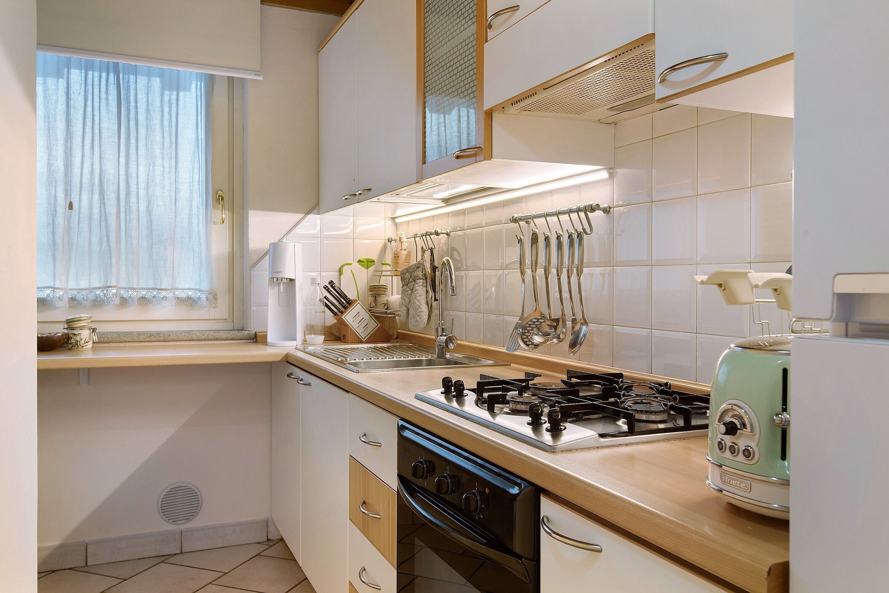 Una cucina con piano cottura a gas, forno, lavello e una finestra con tende.