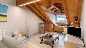 Une pièce de style loft avec un plafond en pente, une table à manger en bois, un canapé, un téléviseur et une cheminée.