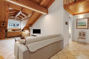 A cozy room with a sofa, a television, wooden beams, a window, and a mirror. - Apartment 'Il Nido' with Mountain View, Wi-Fi and Air Conditioning (Aosta)