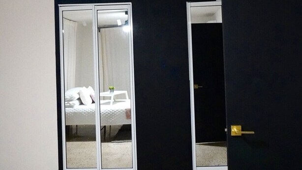 Quarto com cama, ventoinha no teto, guarda-roupa e porta.