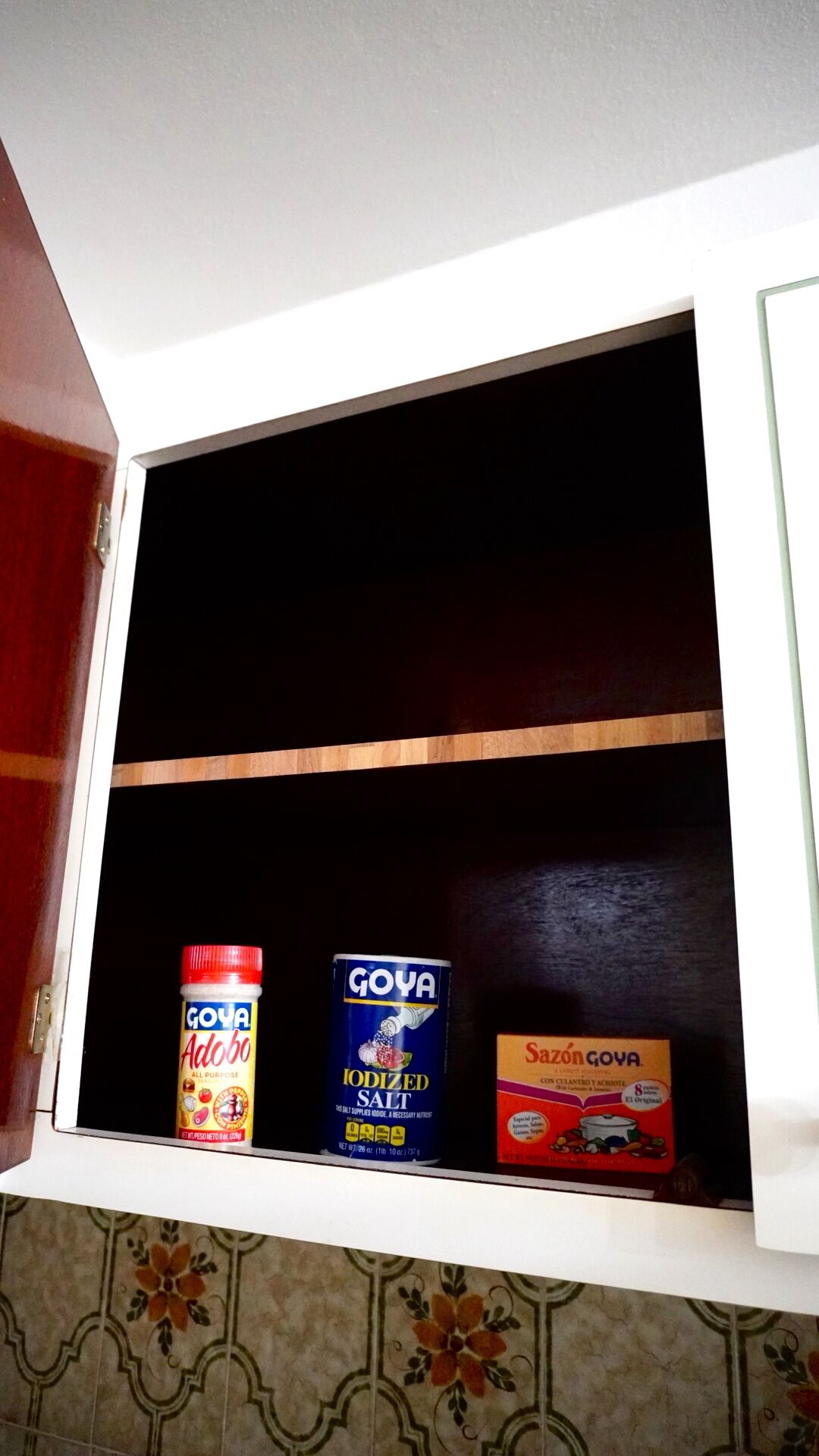 Un armario con tres artículos: una botella de salsa Goya Adobo, una lata de sal yodada Goya y una caja de Sazón Goya.