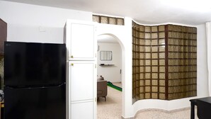 Cozinha compacta com geladeira preta, armários brancos e painel de azulejos.