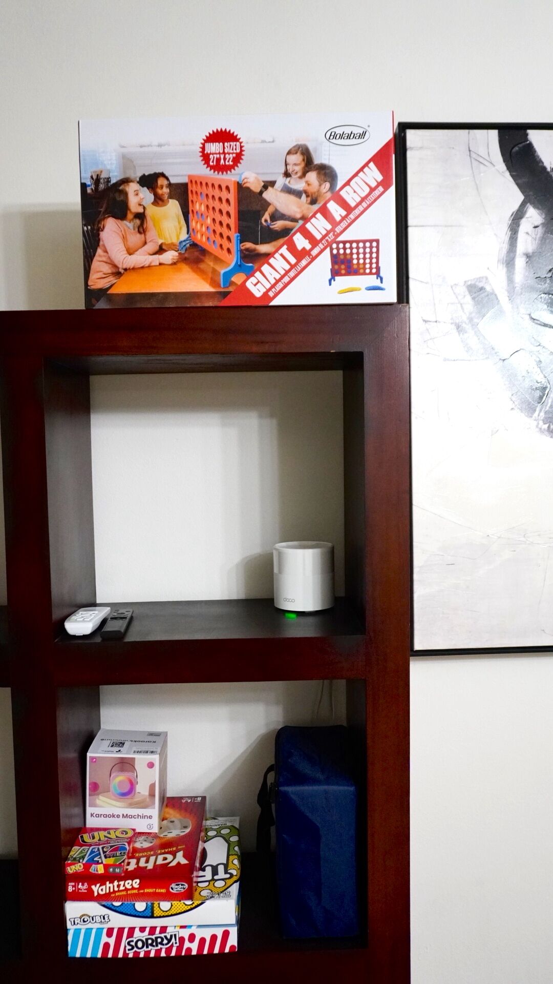 A shelf with a box of a board game, a white mug, and a karaoke machine.