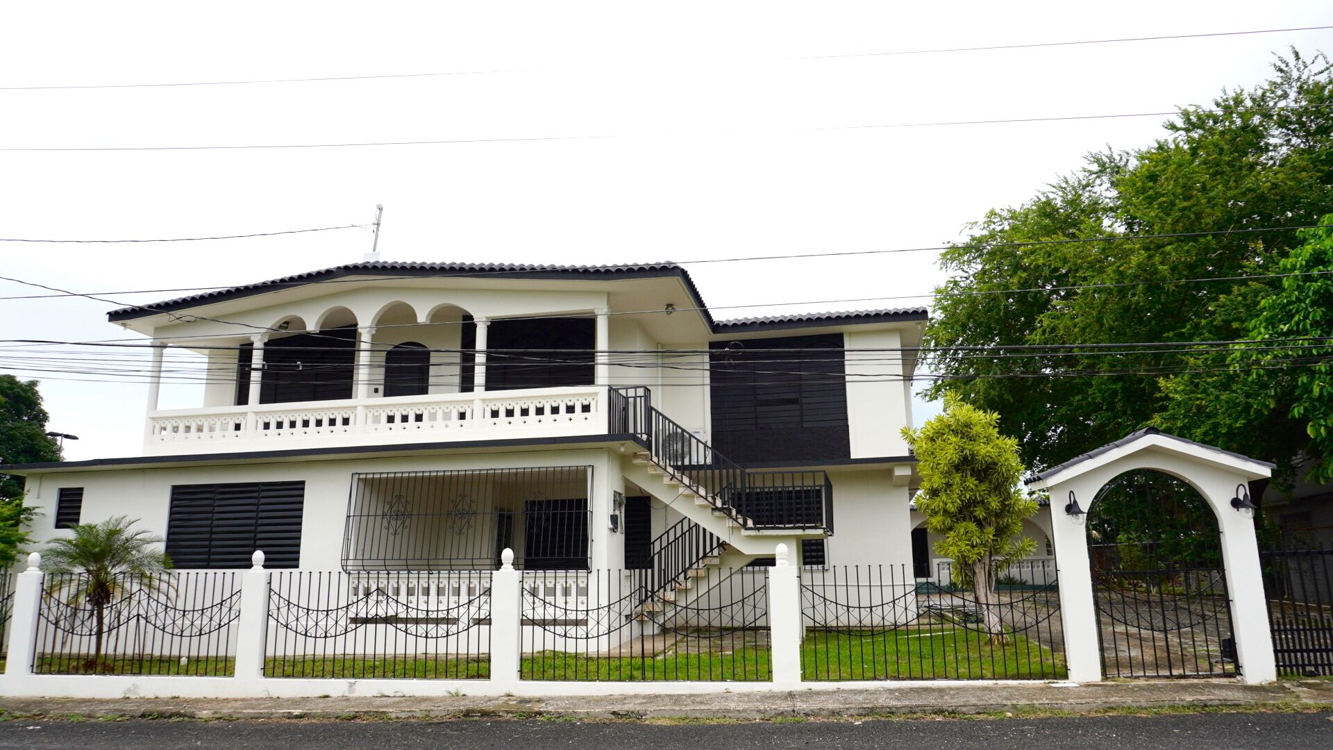 A two-story building with a balcony, a gated entrance, and a staircase leading to the upper floor.