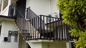 Um edifício de dois andares com varanda, escadaria e aparelho de ar condicionado.