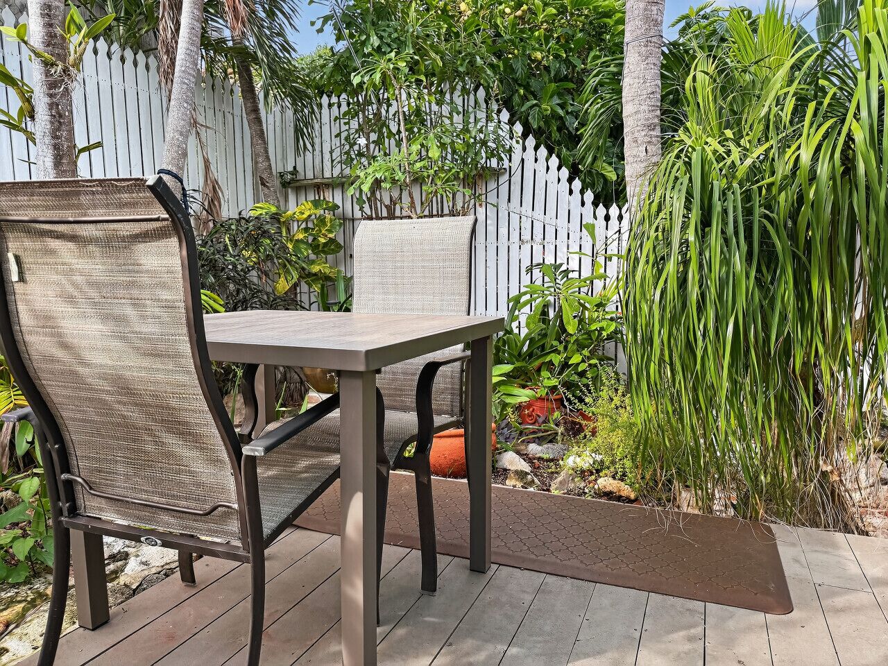 An outdoor patio with a table and chairs, surrounded by a white picket fence and lush greenery.