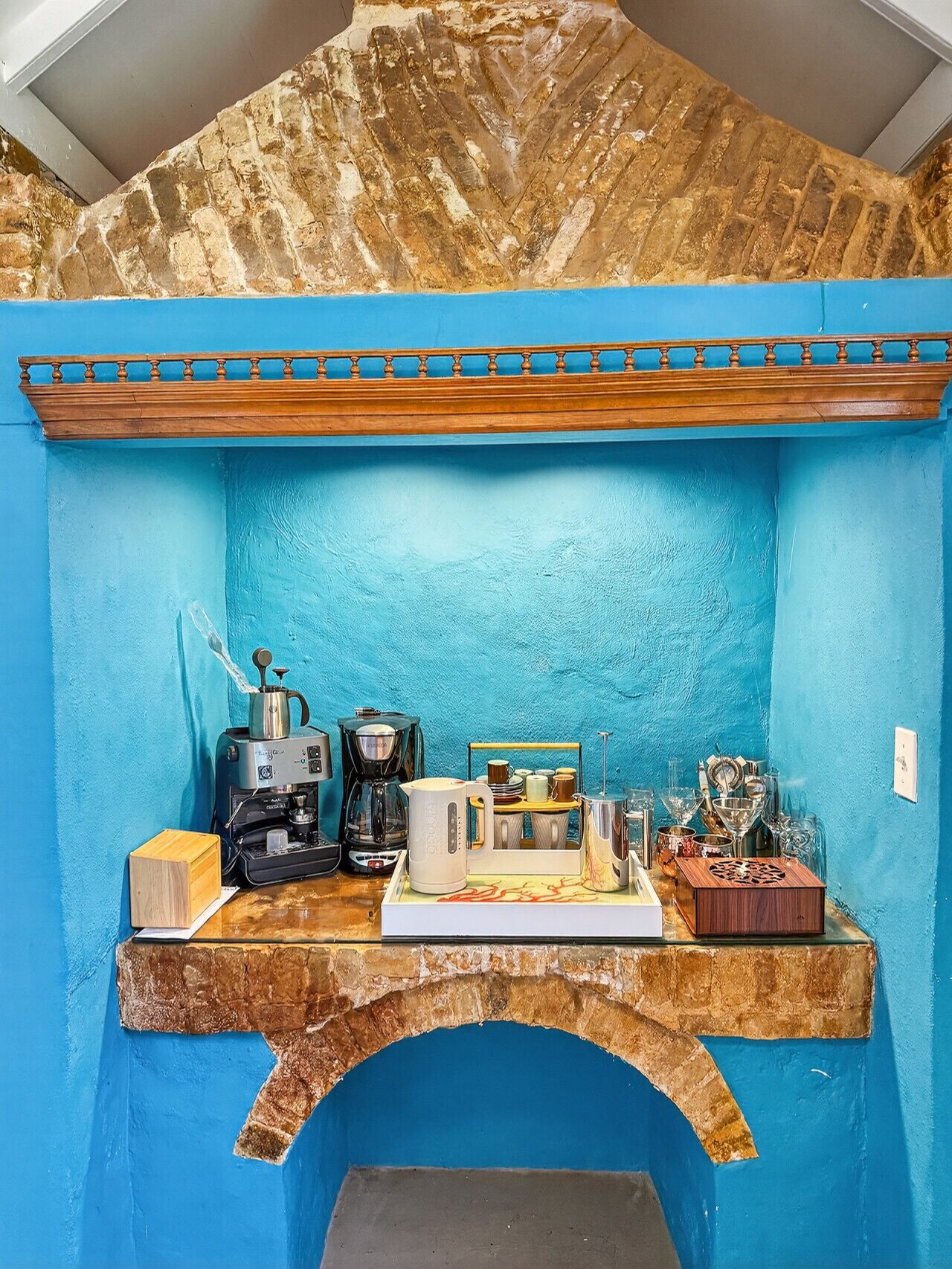 Une pièce aux murs bleus, avec un banc en bois, une machine à café, une bouilloire, ainsi que différentes tasses et mugs.