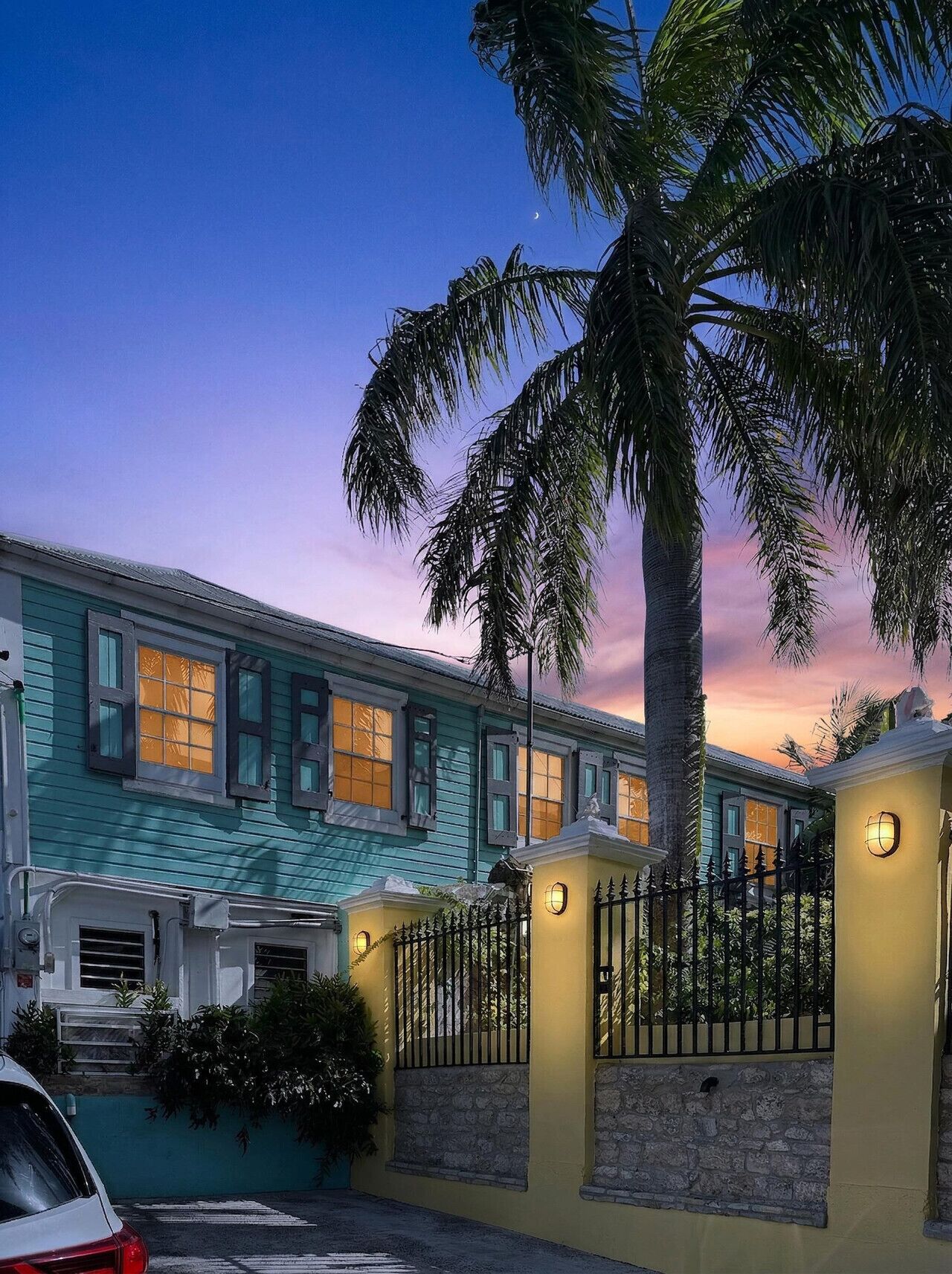 A two-story building with a teal facade, a stone wall, and a palm tree in the foreground.