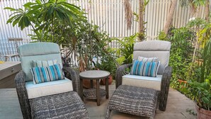 Ein Patio mit Korbmöbeln, darunter zwei Stühle und ein kleiner Tisch.