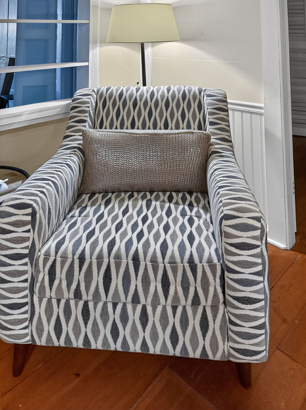 Une chaise recouverte d’un tissu à motifs zébrés, accompagnée d’un coussin assorti, placée dans une pièce dotée d’une fenêtre et d’une lampe.