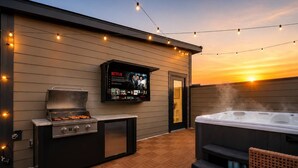 Un patio exterior con una parrilla, un jacuzzi y una pantalla de televisión que muestra una serie de Netflix.