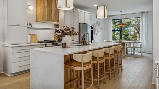 Una cocina moderna con armarios blancos, una isla de mármol y taburetes de madera.