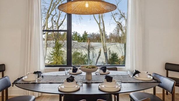 A dining area with a round table set for four, a large window with a view of trees and a building, and a woven pendant light above the table. - NEW Modern Nashville Escape with Rooftop Hot Tub (Nashville)