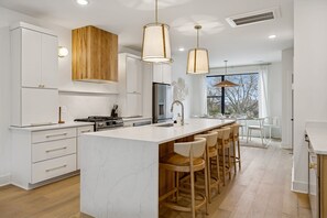 Une cuisine moderne avec des meubles blancs, un îlot en marbre et des luminaires suspendus.