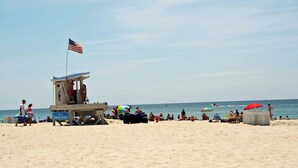 A lifeguard tower with an American flag, beach umbrellas, and people on the sand. - Molly's Beachside Cottage 3BR 2BA Almost Oceanfront in Atlantic Beach (Atlantic Beach)