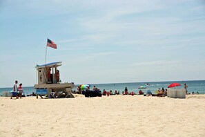 Ein Rettungsschwimmturm mit US-amerikanischer Flagge, Strandsegeln und Menschen am Sandstrand.
